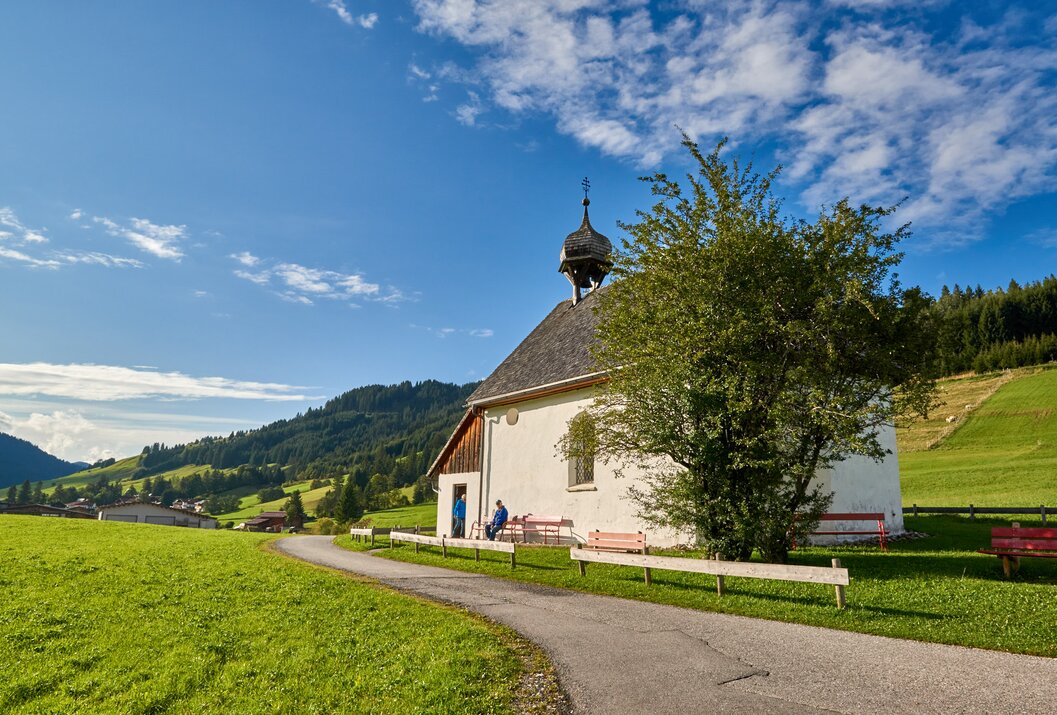 Kleine Kapelle auf grüner Wiese vor Berglandschaft unter blauem Himmel