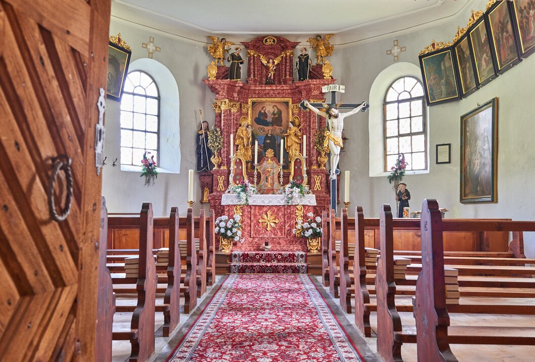 Innenansicht einer Kirche mit Altar, Kruzifix, rotem Teppich und Kirchenbänken