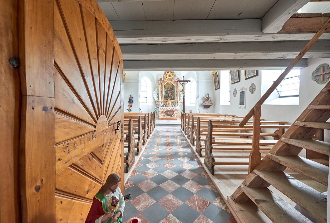 Blick in eine Kirche durch eine geöffnete Holztür mit Jesusstatue im Vordergrund