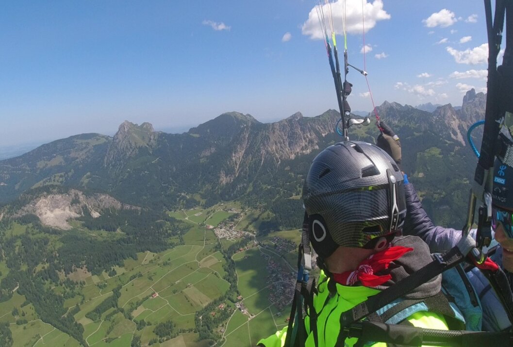 Gleitschirmflieger vor Berglandschaft mit grünen Wiesen und blauem Himmel