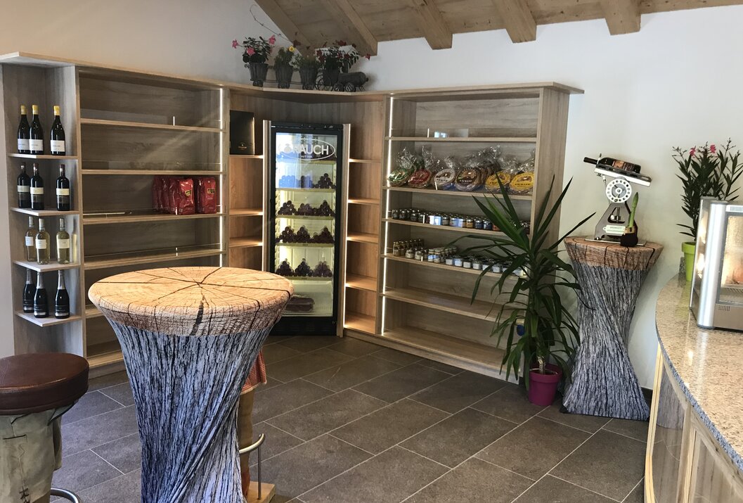 Innenansicht eines Verkaufsraums mit Regalen, Kühlschrank, Dekoration und zwei Stehtischen mit Holzoptik