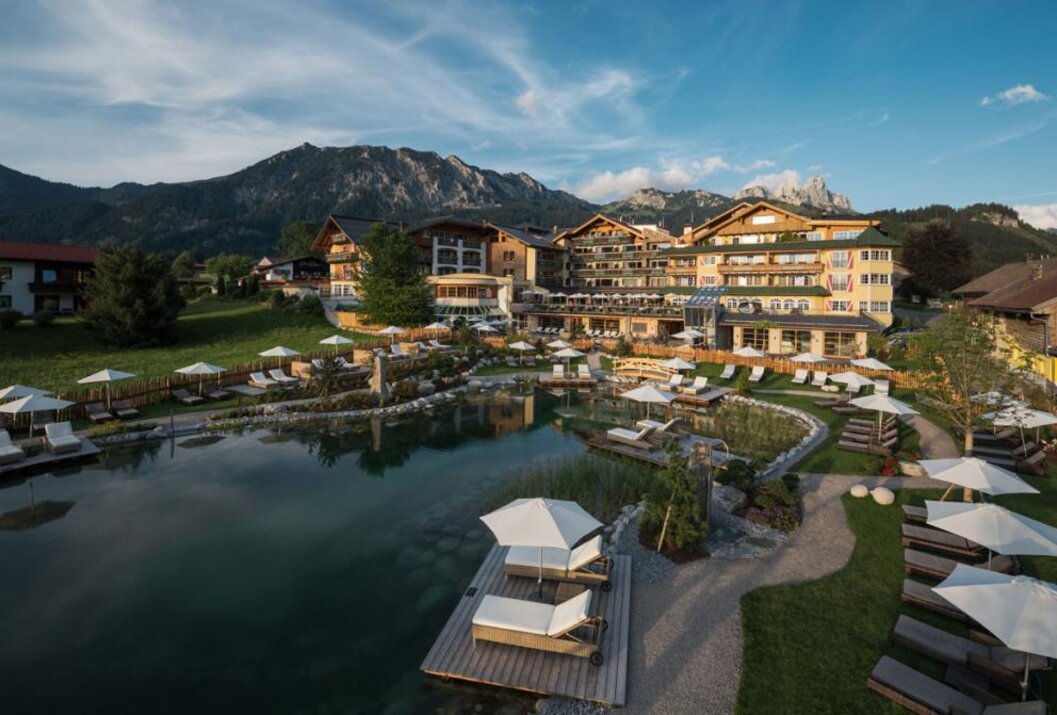 Hotelanlage am See mit Liegen und Bergpanorama