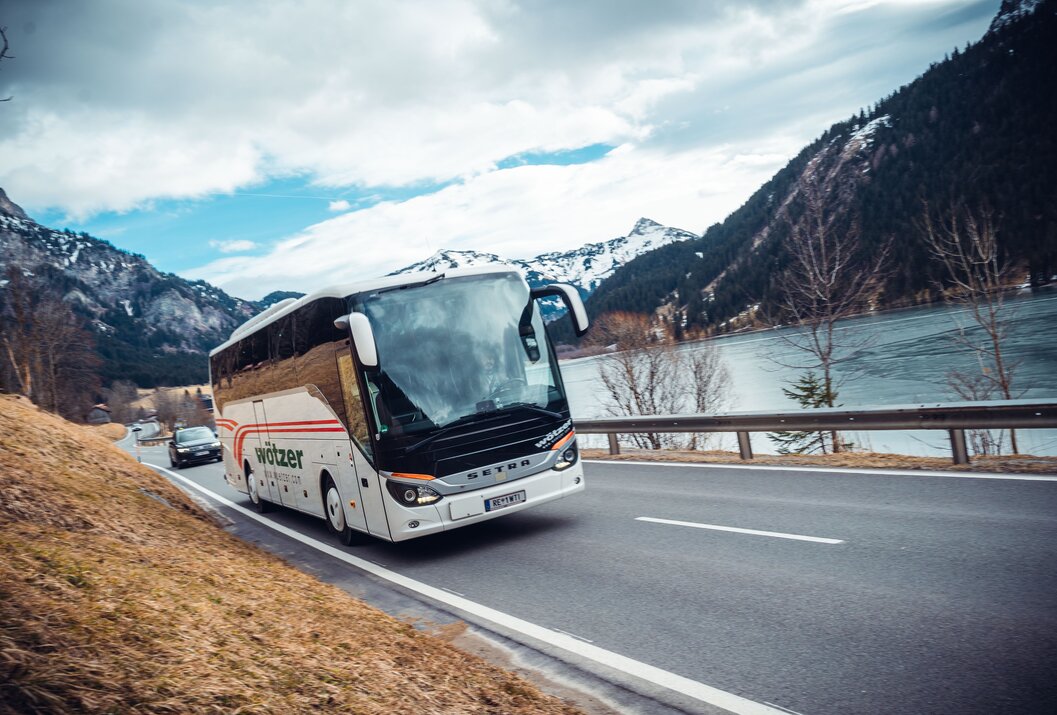 Weißer Reisebus fährt auf Straße vor Bergkulisse