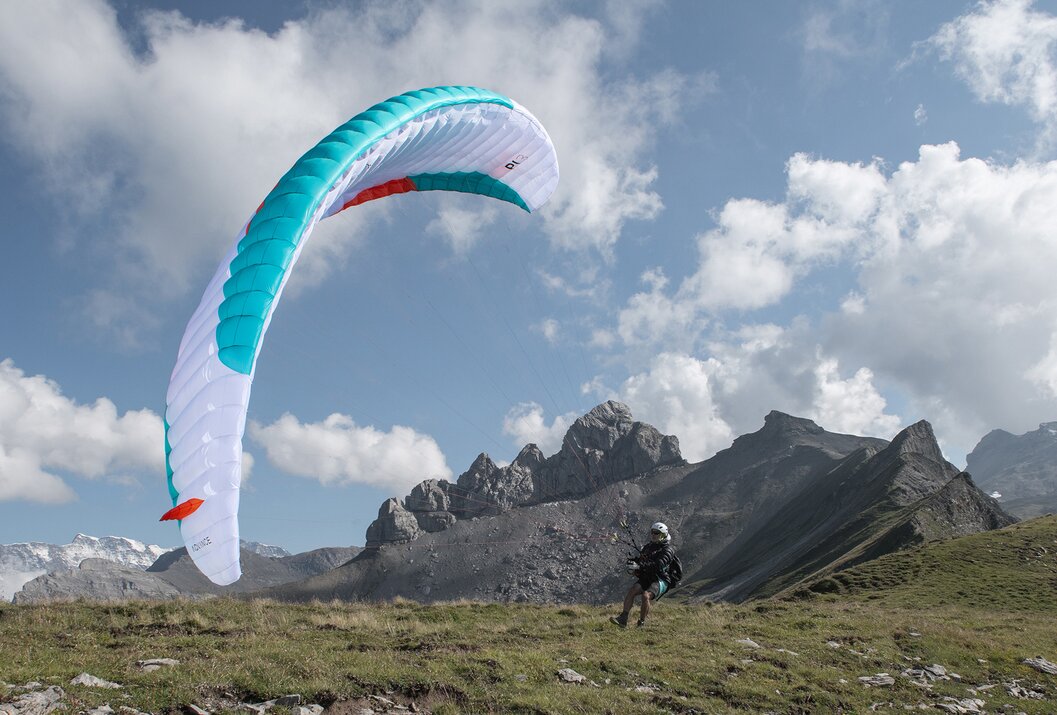 Gleitschirmflieger startet vor Bergkulisse mit blau-weißem Schirm