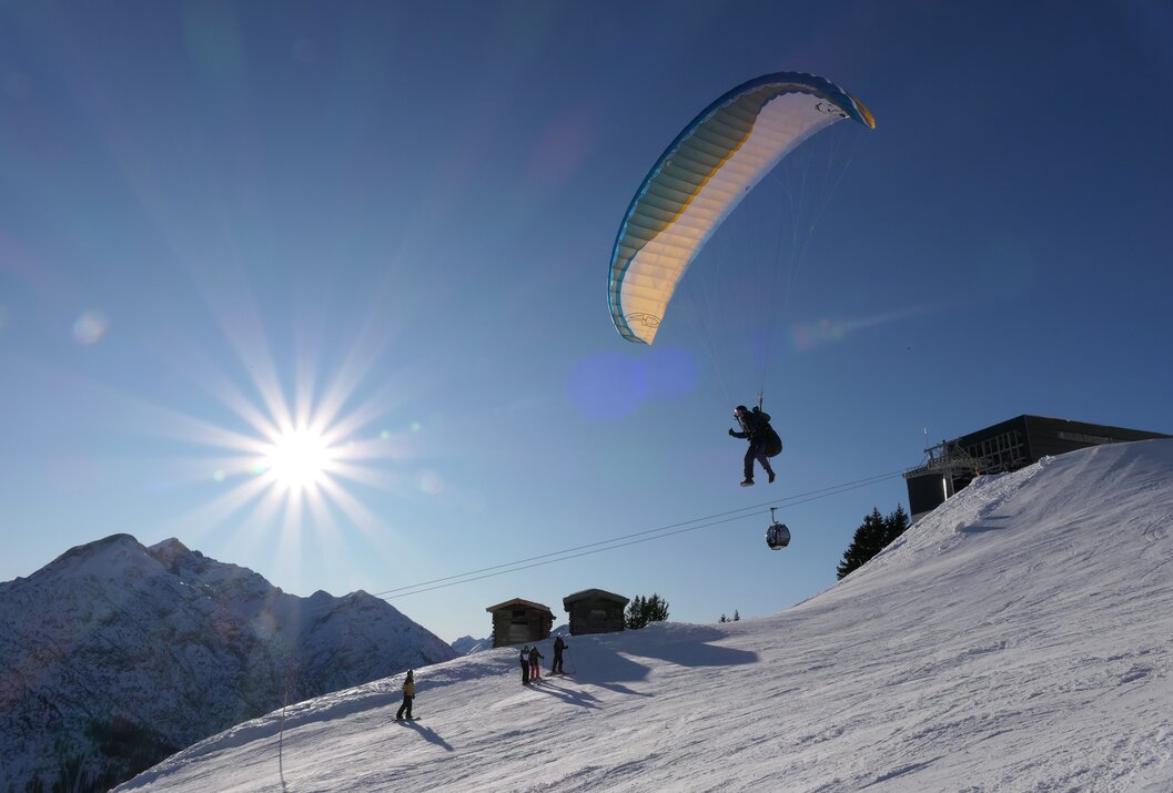 Gleitschirmflieger über schneebedeckter Piste vor blauem Himmel und strahlender Sonne