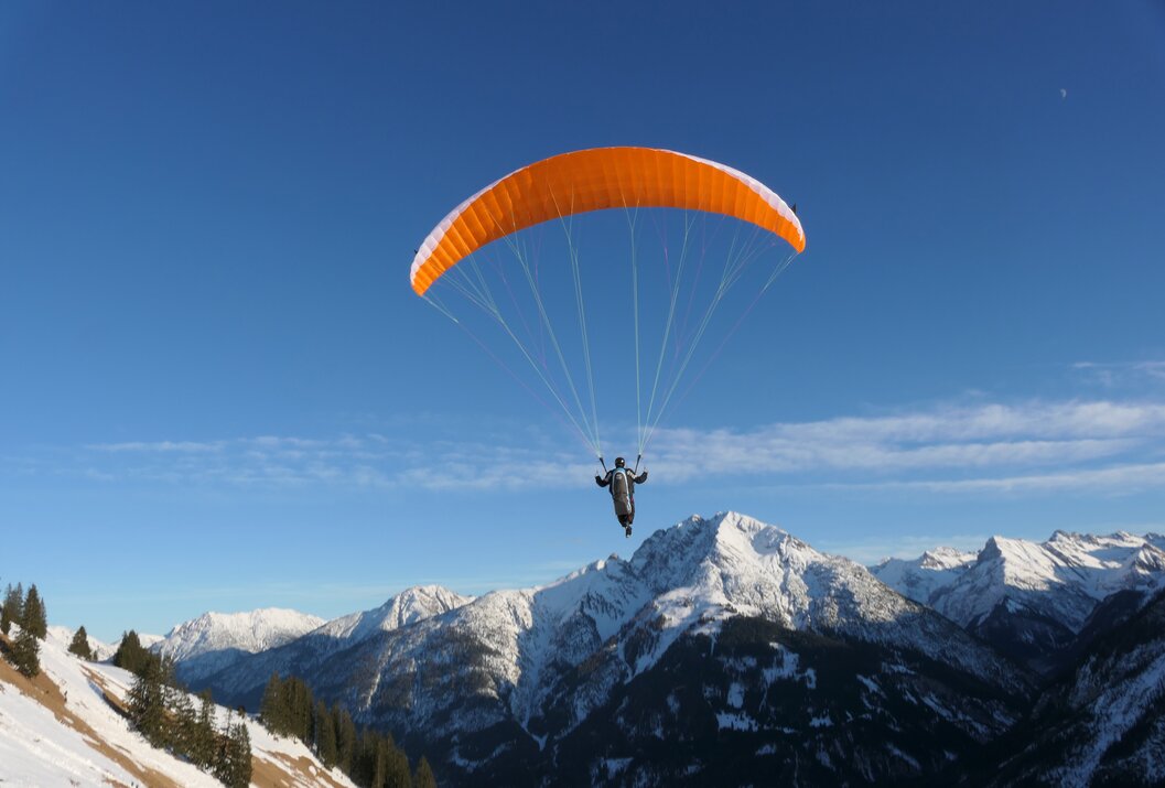 Gleitschirmflieger vor schneebedeckten Bergen unter blauem Himmel