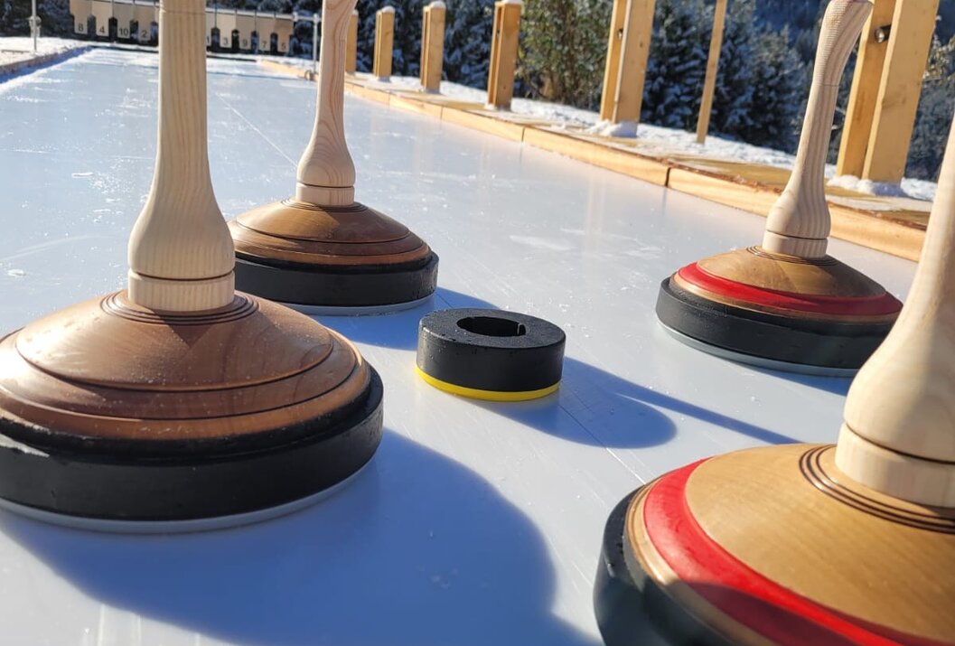 Eisstockschießen mit Eisstöcken und Daube auf Eisfläche vor verschneiter Berglandschaft