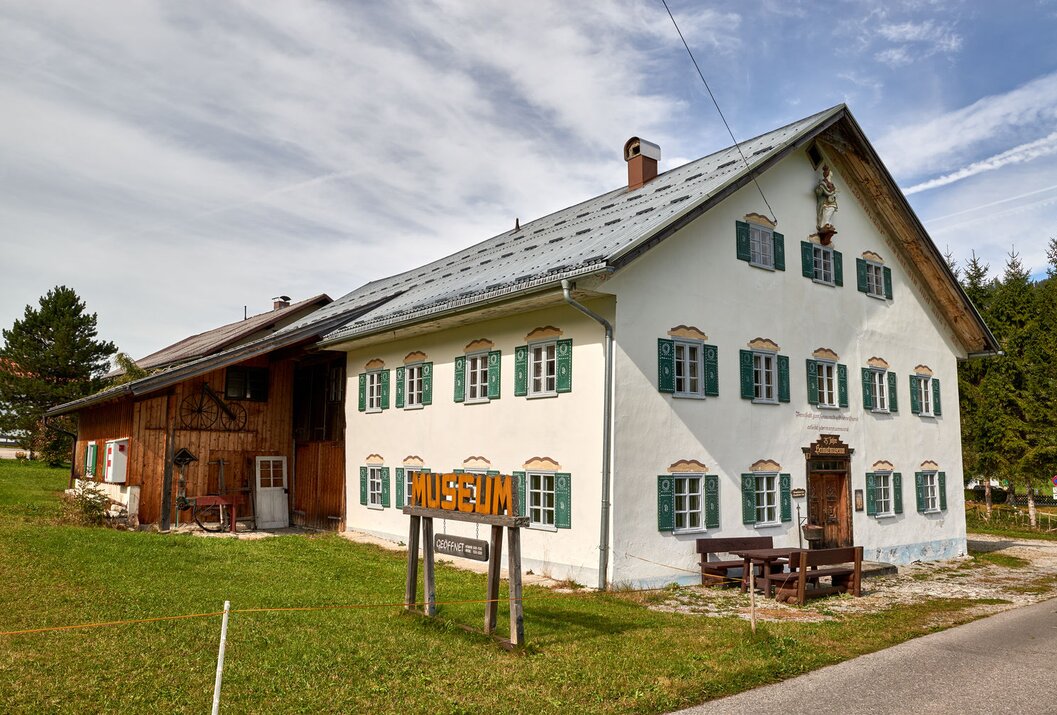 Weißes Haus mit grünen Fensterläden und Museumsschild im Vordergrund
