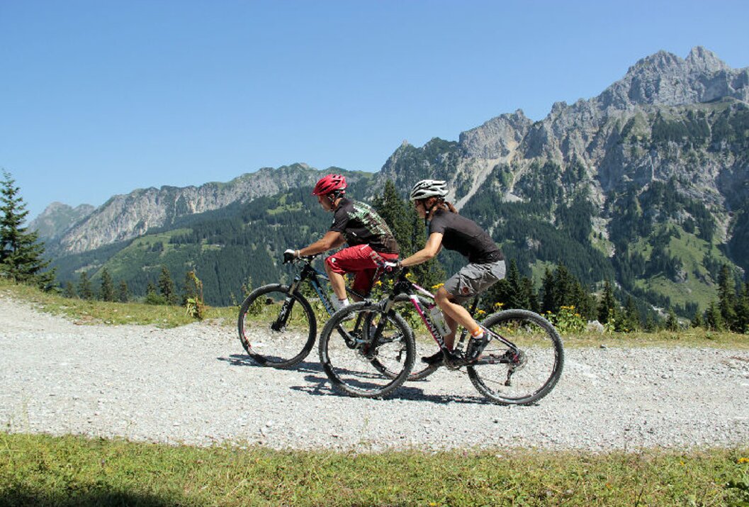 Zwei Mountainbiker fahren auf Schotterweg vor Bergkulisse