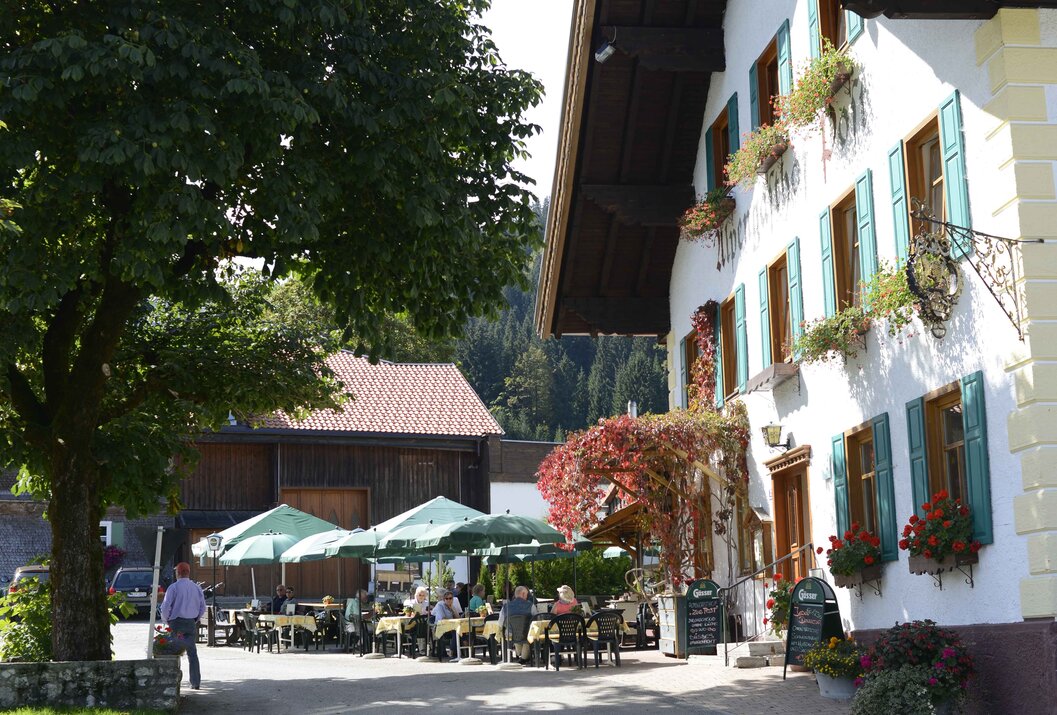 Gasthof mit grünen Fensterläden und Außenterrasse unter Sonnenschirmen
