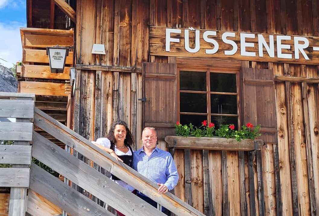 Paar vor Holzhaus "Füsseni" mit Fenster und Blumenkasten auf Treppe