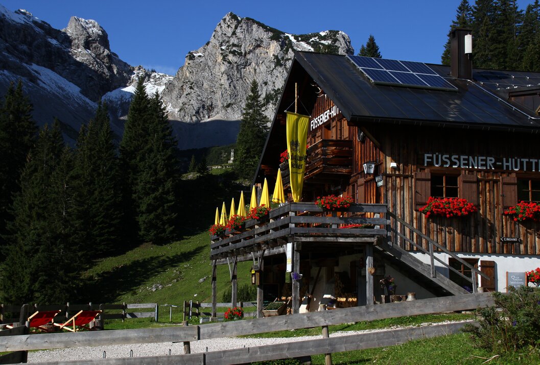 Hütte mit gelbem Banner vor Bergkulisse und blauem Himmel