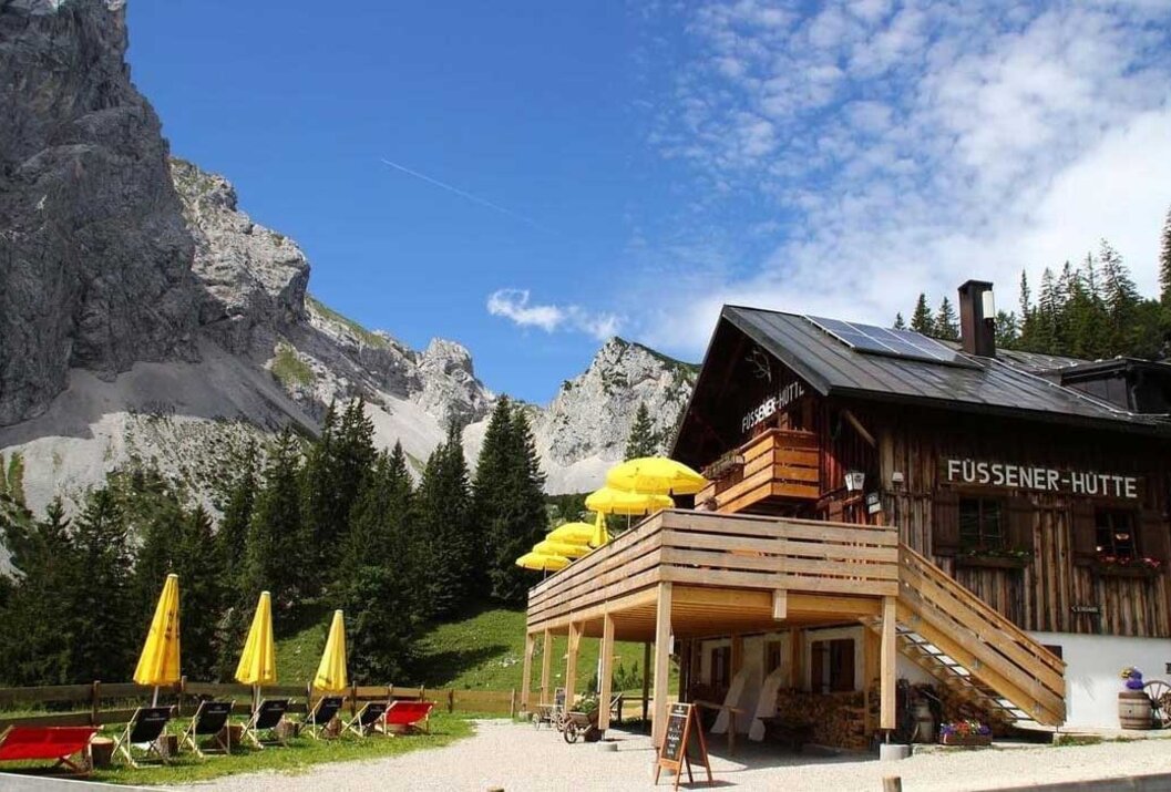 Berghütte mit gelben Sonnenschirmen vor Bergkulisse und blauem Himmel