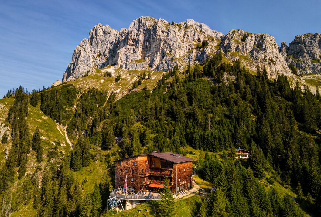 Hütte vor Berglandschaft mit Wald und blauem Himmel