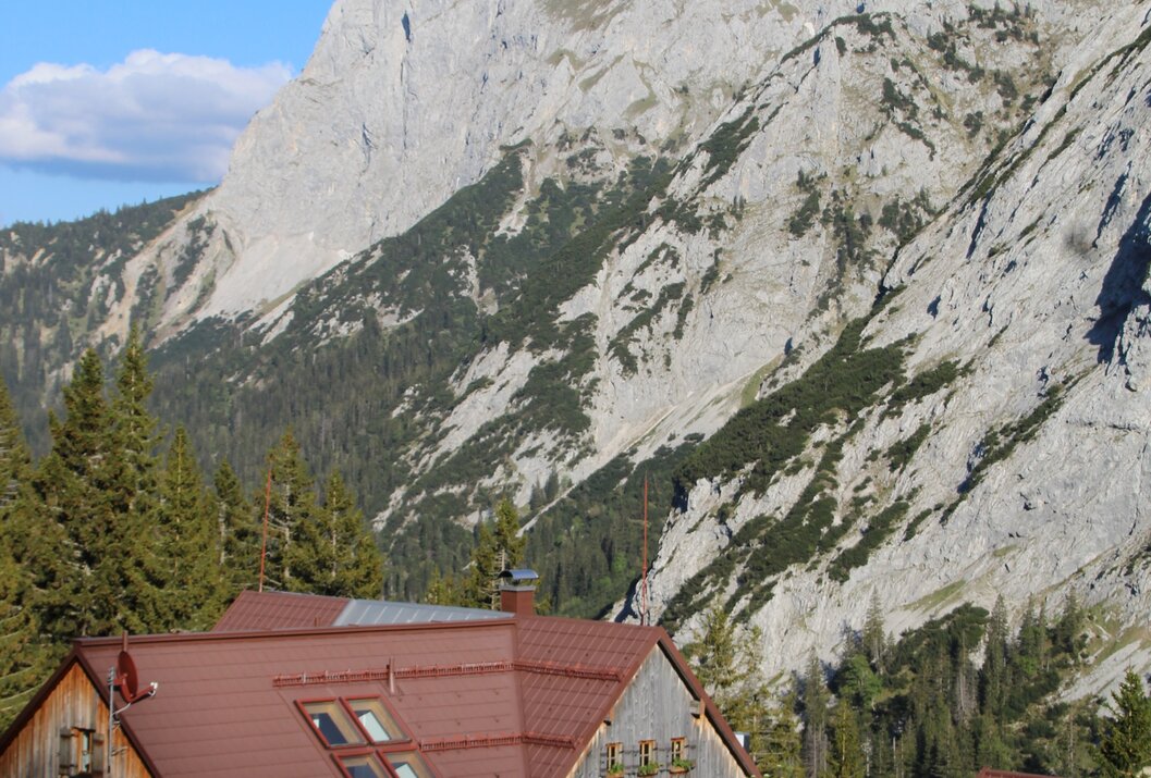 Hütte vor felsigem Bergmassiv unter blauem Himmel