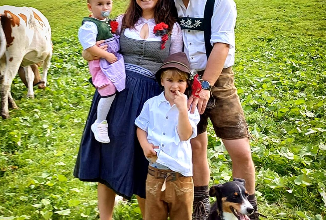 Familie in Tracht auf grüner Wiese mit Kühen und Hund