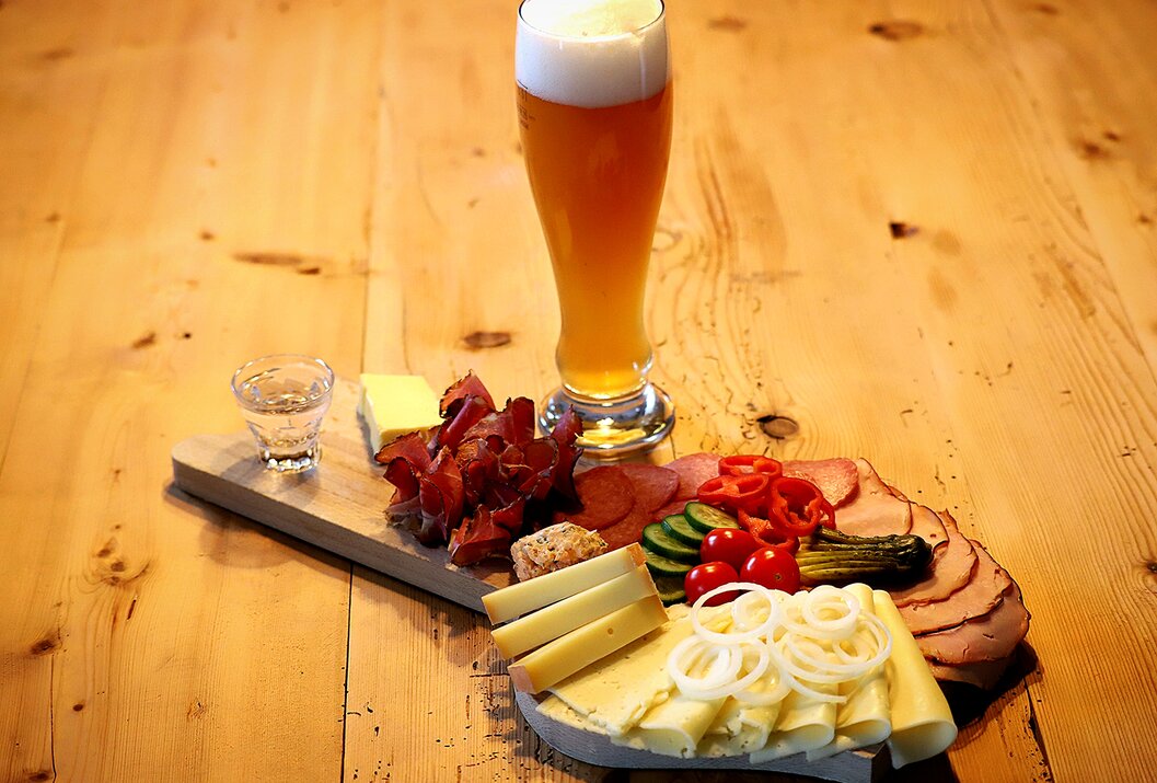 Bier, Schnaps und Brotzeitplatte mit Wurst, Käse, Zwiebeln und Gurken auf Holztisch