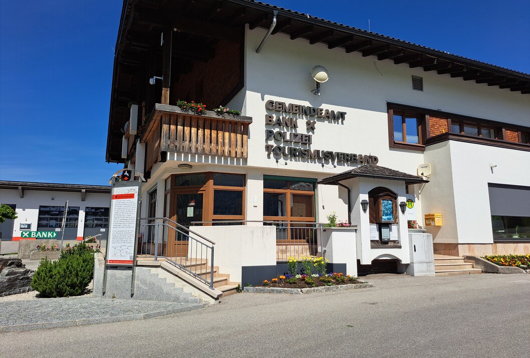 Gebäude mit Aufschrift Gemeindeamt Bank Polizei Tourismusverband unter blauem Himmel