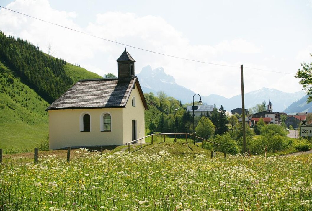 Kleine Kapelle auf einer Wiese vor Hügeln und Bergen an einem sonnigen Tag