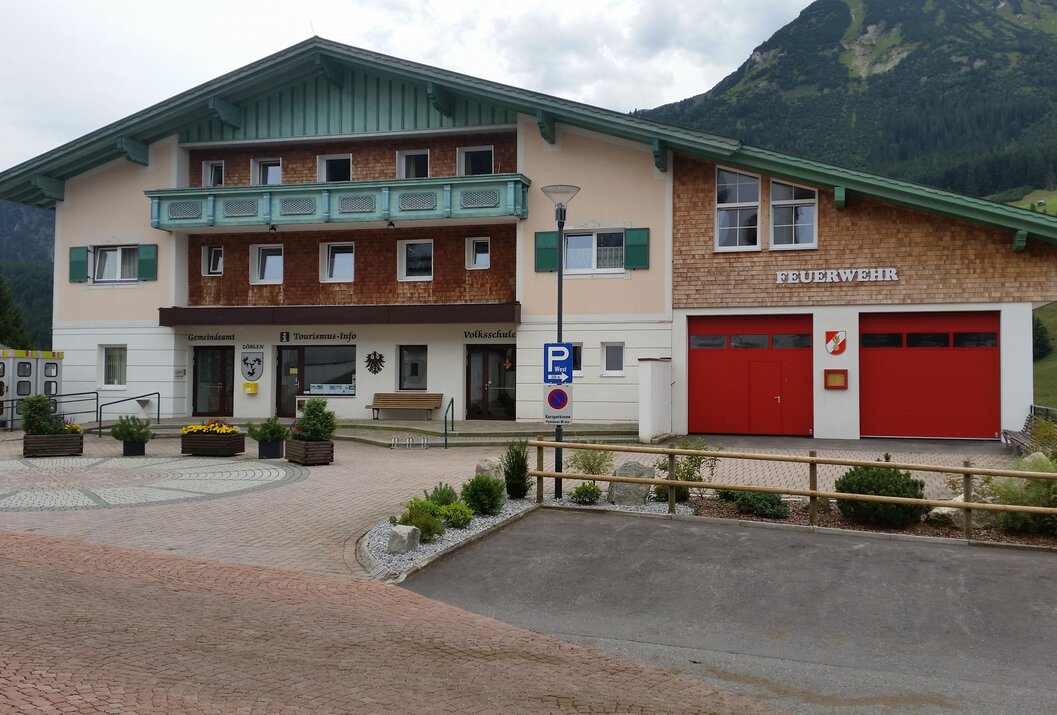 Gebäude mit Bankfiliale, Tourismusbüro und Feuerwehrhaus vor Bergkulisse