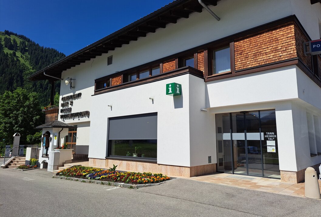Weißes Gebäude mit braunen Akzenten und Blumenbeet im Vordergrund