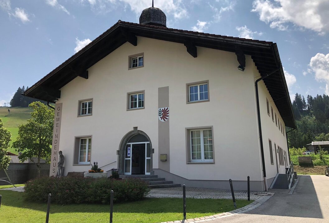 Weißes Gemeindehaus mit dunklem Dach und Wappen an der Fassade