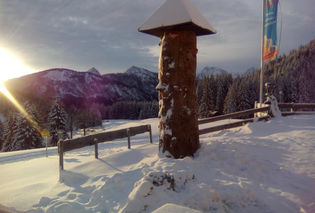 Holzsäule mit Dach im Schnee vor Berglandschaft