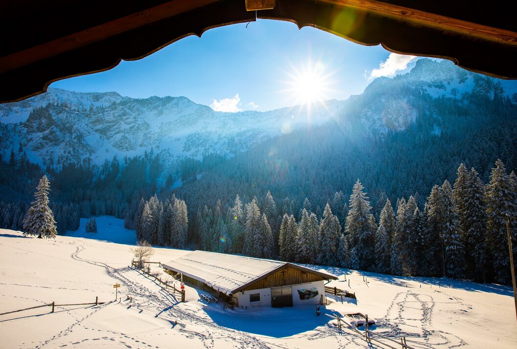 Winterlandschaft mit schneebedeckten Bergen, Wald und Hütte unter blauem Himmel