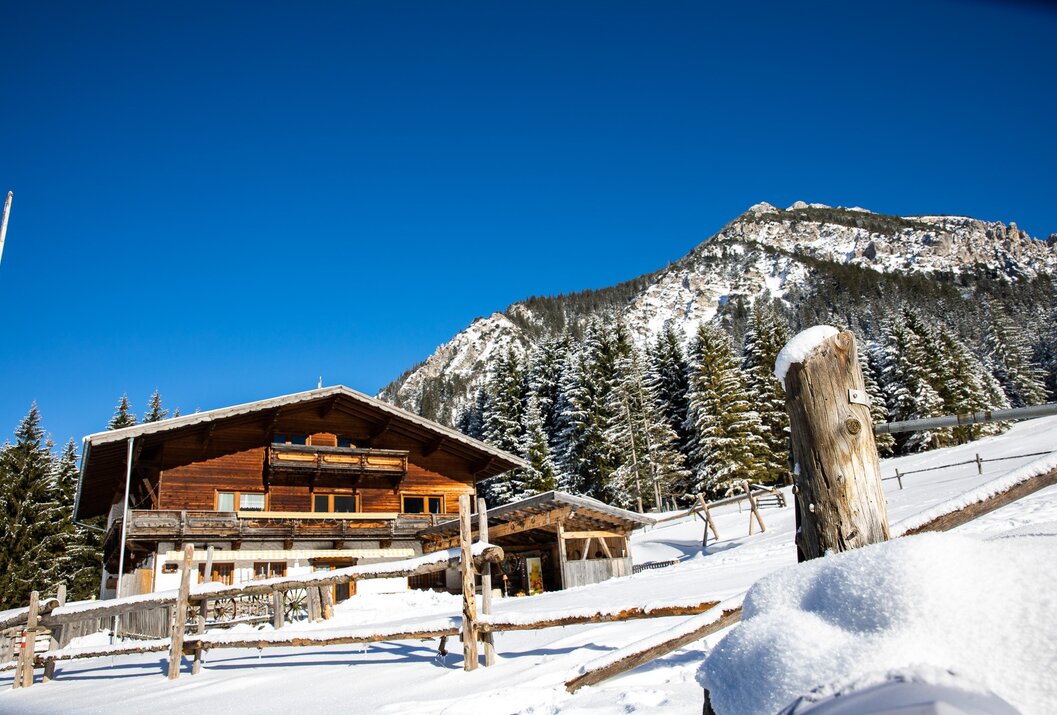 Holzhütte im Schnee vor Berg und blauem Himmel