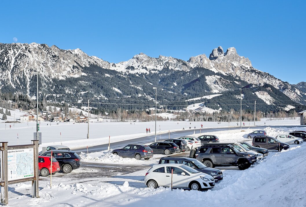 Verschneiter Parkplatz mit Autos vor schneebedeckten Bergen unter blauem Himmel