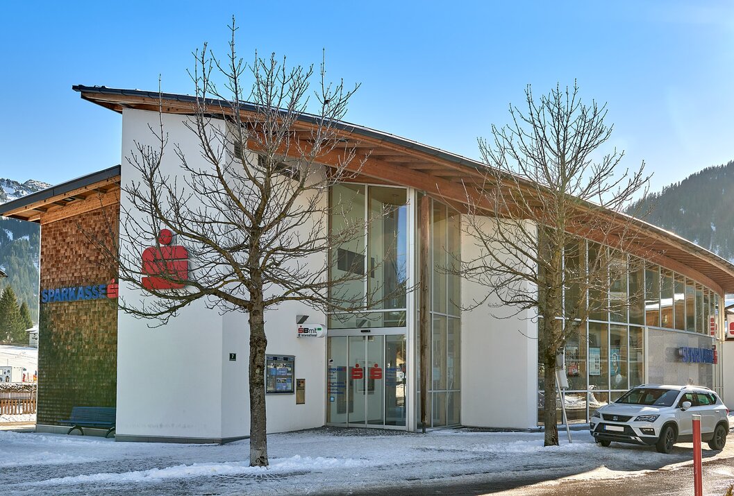 Sparkasse-Filiale mit Glasfassade und Bäumen davor an einem sonnigen Tag