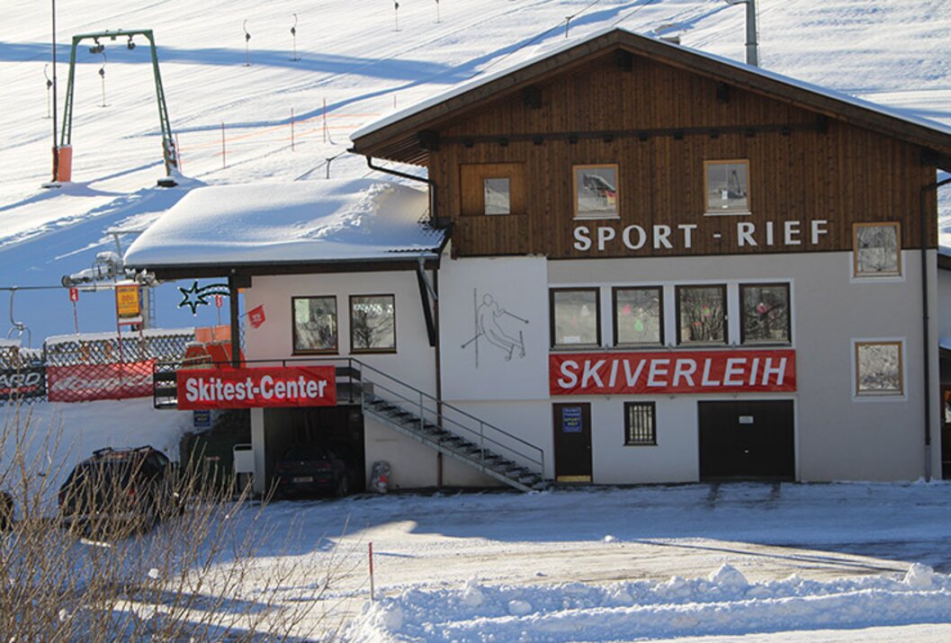 Gebäude mit Skiverleih und Skitest-Center im Schnee vor einer Skipiste