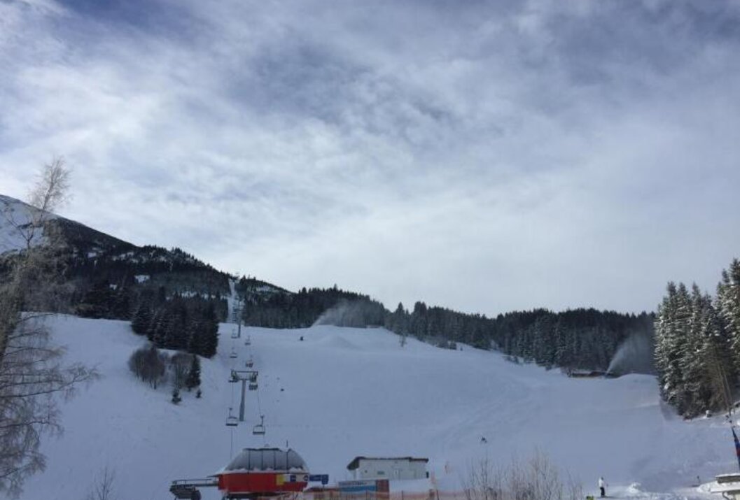 Verschneite Skipiste mit Liftanlagen und Schneekanonen unter bewölktem Himmel
