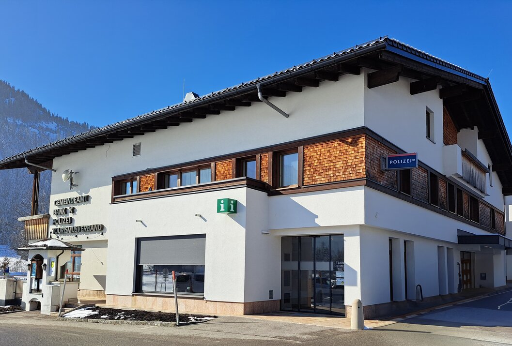 Weißes Gebäude mit braunen Holzelementen und blauem Polizeischild unter blauem Himmel