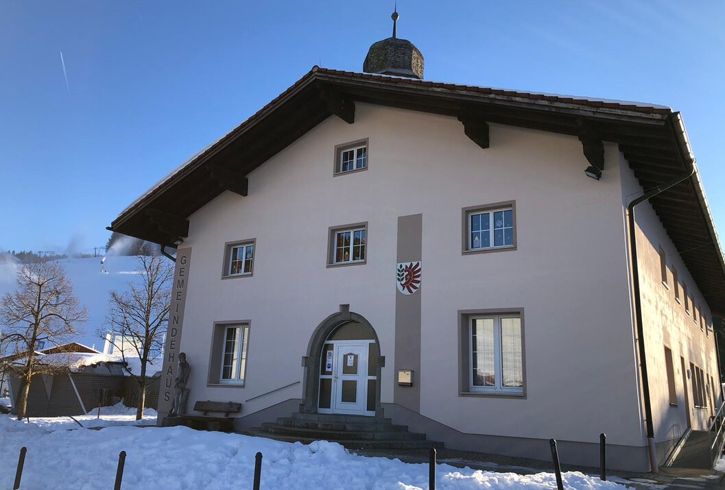 Helles Gebäude mit braunem Dach und Wappen im Winter vor blauem Himmel
