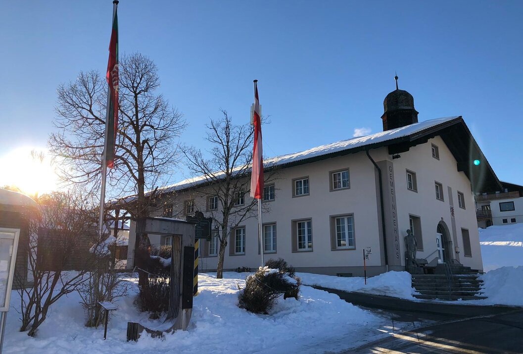 Weißes Gebäude mit Schnee, zwei Fahnenmasten und blauem Himmel