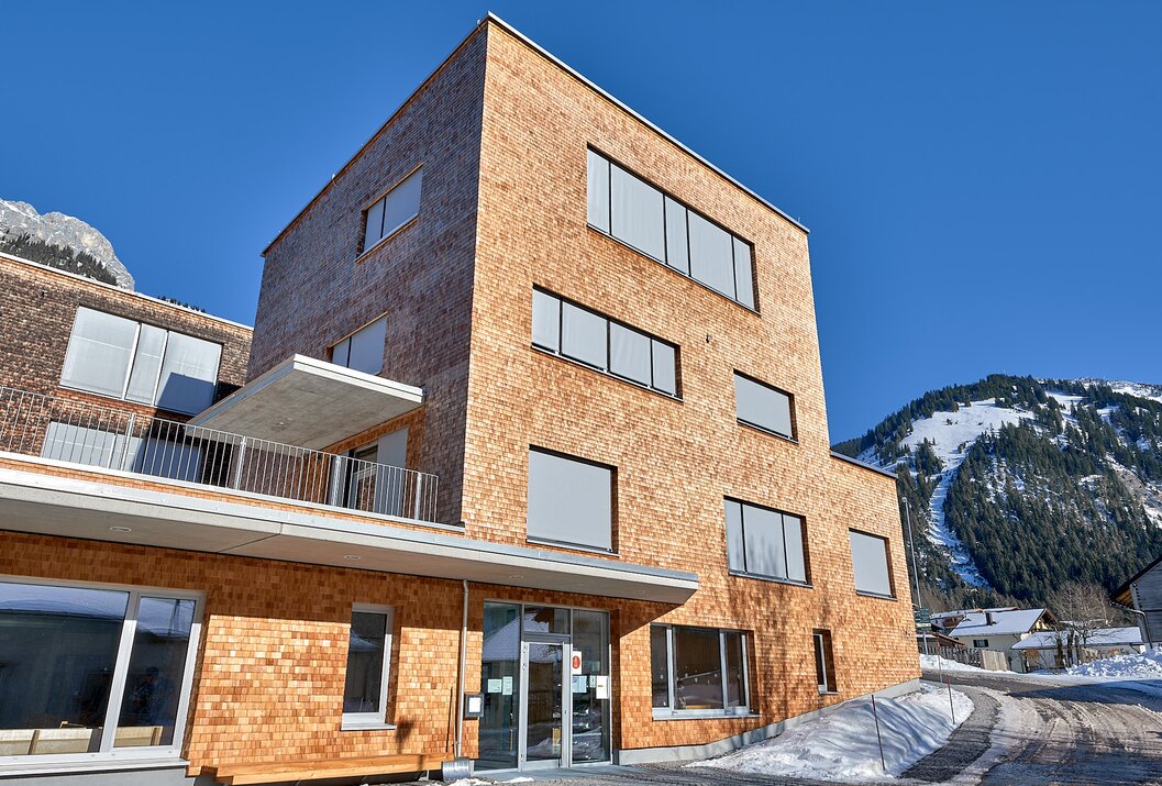 Holzverkleidetes Gebäude mit großen Fenstern vor blauem Himmel und Bergkulisse