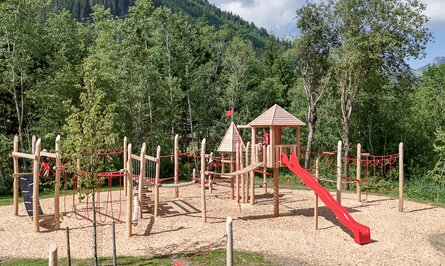 Playground with slide and climbing frame in front of a wooded mountain