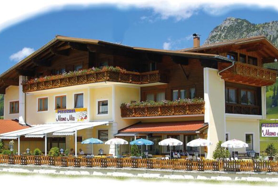 Gelbes Hotel mit Balkonen und Restaurant im Freien vor Bergkulisse
