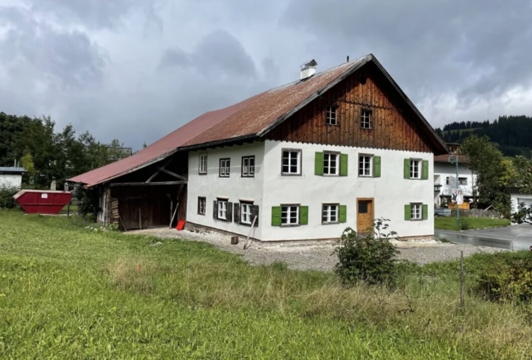 Bauernhaus mit braunem Dach und grünen Fensterläden auf einer grünen Wiese