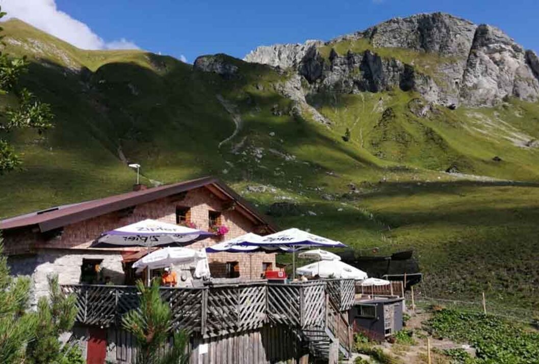 Rustic alpine hut with terrace in front of green mountains