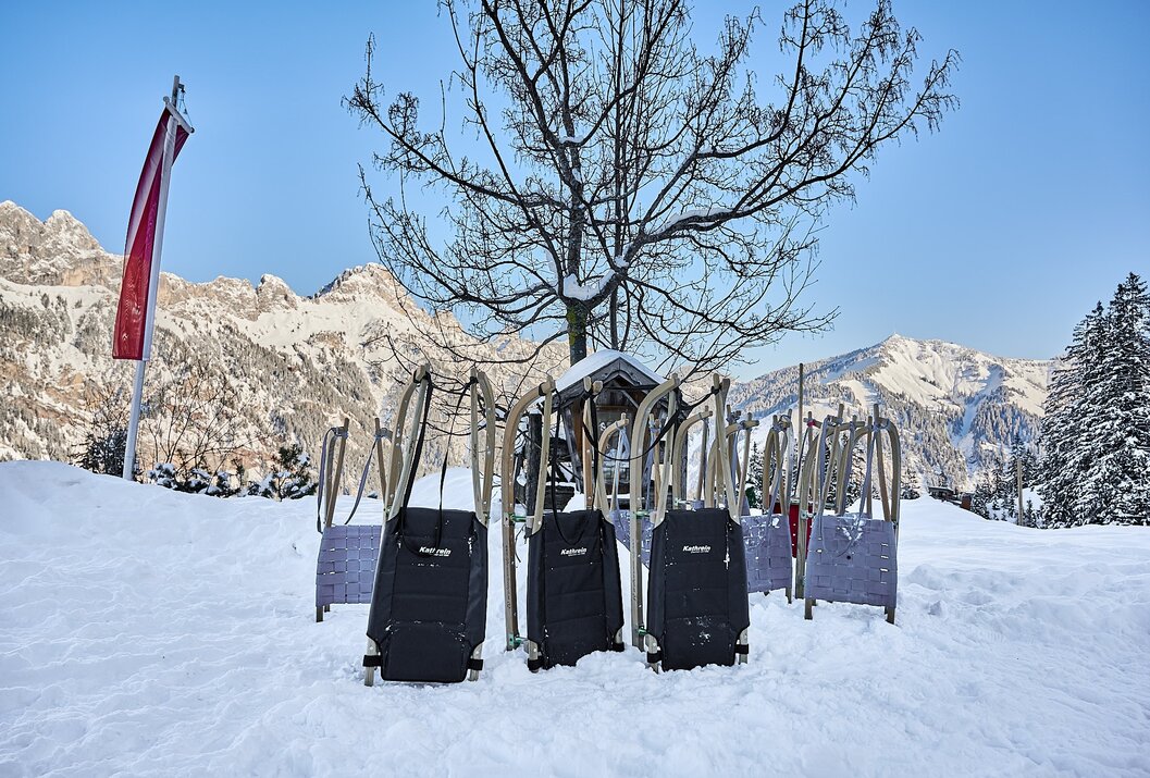 Mehrere Holzrodel im Schnee vor verschneiten Bergen
