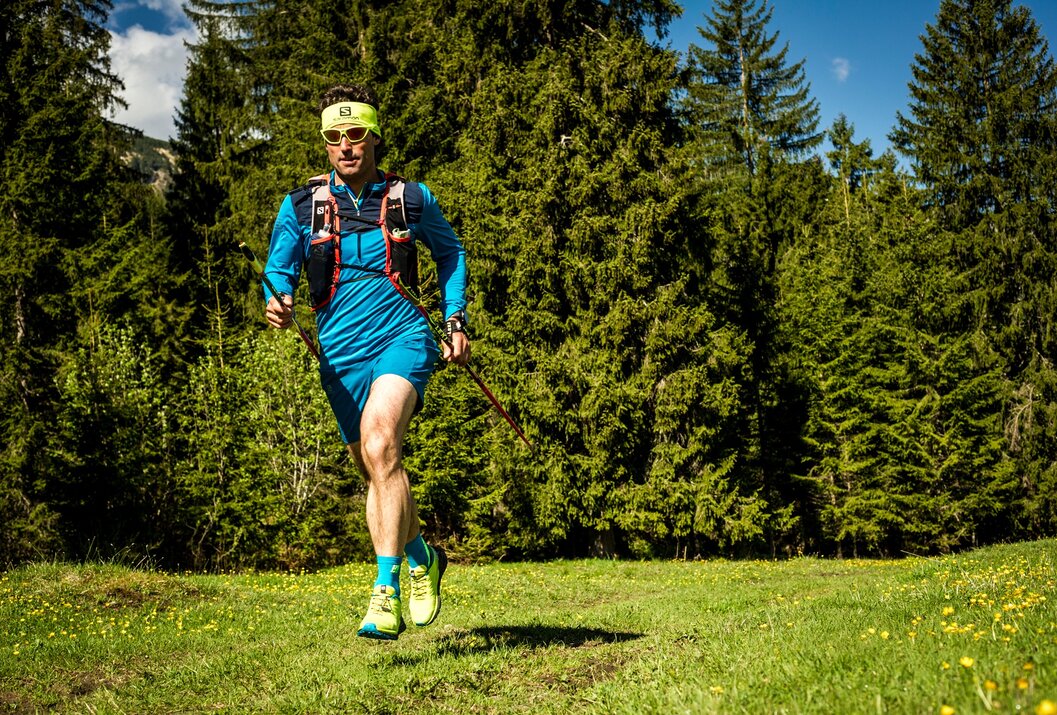 Trailrunner mit Stöcken auf sonniger Waldlichtung