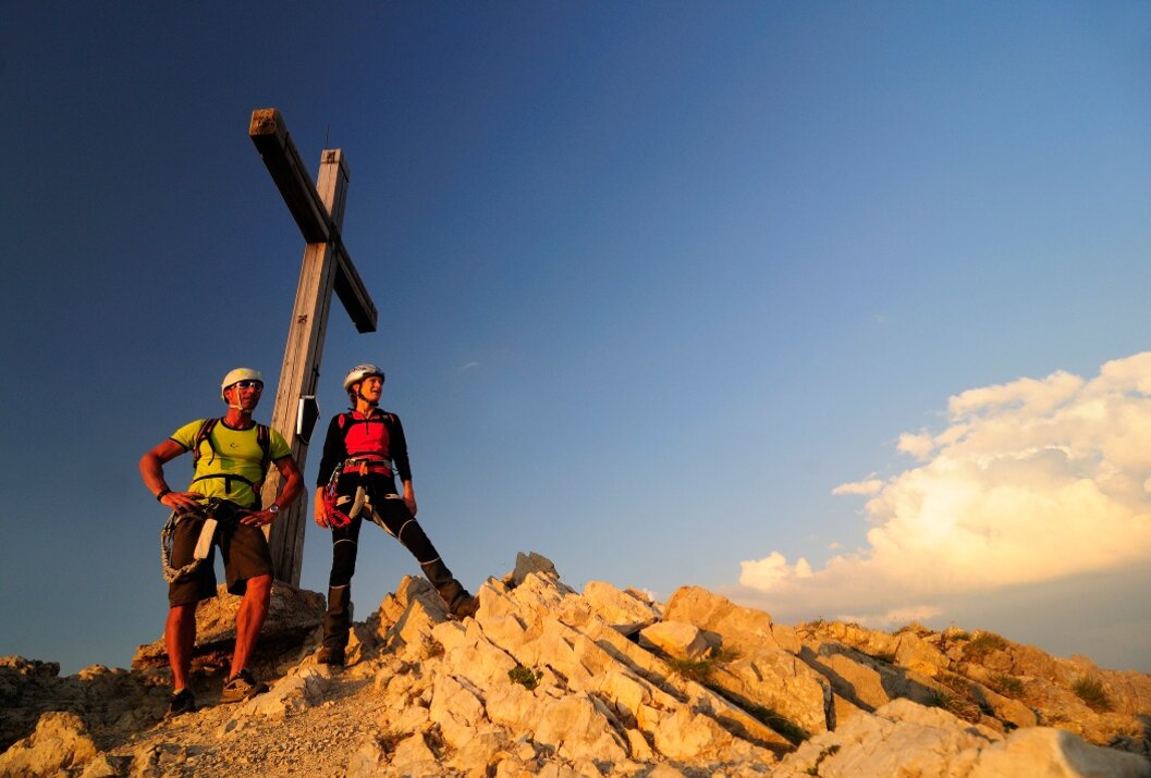 Two mountaineers at the summit cross in the evening sun
