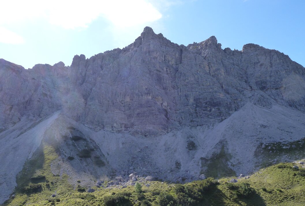 Sun-drenched gray rock mountains above green slopes